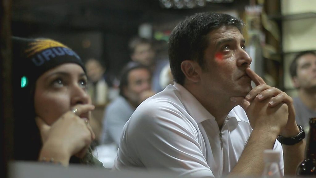 hinchas mirando serios un partido de Uruguay en la TV de un bar fútbol uruguayo