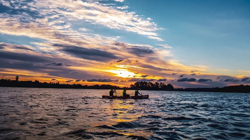 Imagen de tres personas navegando al atardecer sobre una canoa en el río