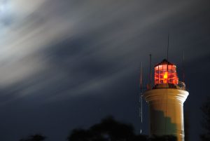 Imagen de la cima de un faro, en una noche nublada. La luz del faro es roja