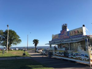 Imagen del carro de tortas fritas de "Pepe, el Rey de las Tortas Fritas". En el frente tiene imágenes de atractivos turísticos del Uruguay, y sobre el techo, una marquesina con una corona de luces de colores. Detrás del carro, el Río de la Plata.