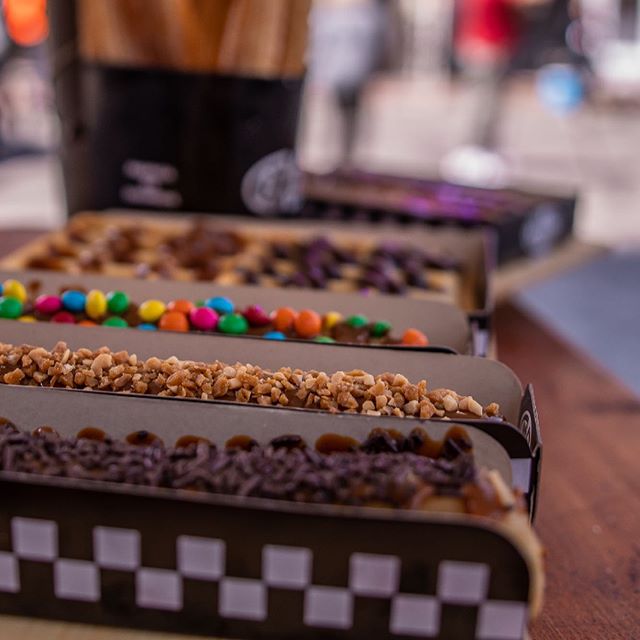 Imagen de varios churros rellenos con distintos toppings, presentados en cajas de cartón individuales a cuadros blancos y negros