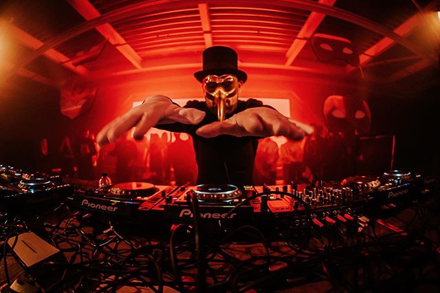 Imagen de un hombre con galera y una máscara dorada con nariz puntiaguda, con las manos extendidas sobre una bandeja de discos