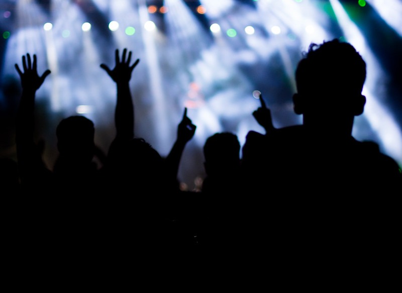Imagen de una multitud de personas bailando en una fiesta electrónica. Se observan siluetas de personas alzando sus brazos; en el fondo, luces y humo.