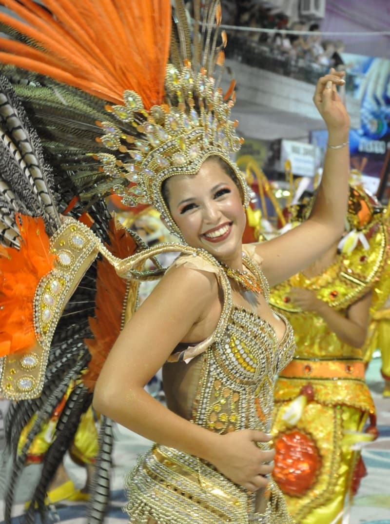 Una vedette, con un diosfraz con plumas naranjas baila y sonríe