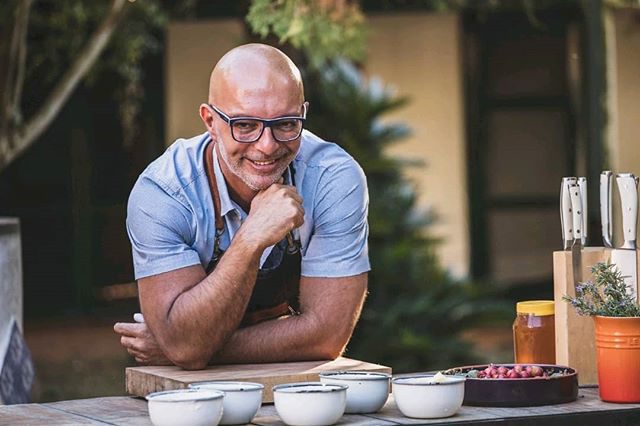Imagen de Hugo Soca mirando a la cámara, atrás de una mesa sobre los cuales hay varios alimentos