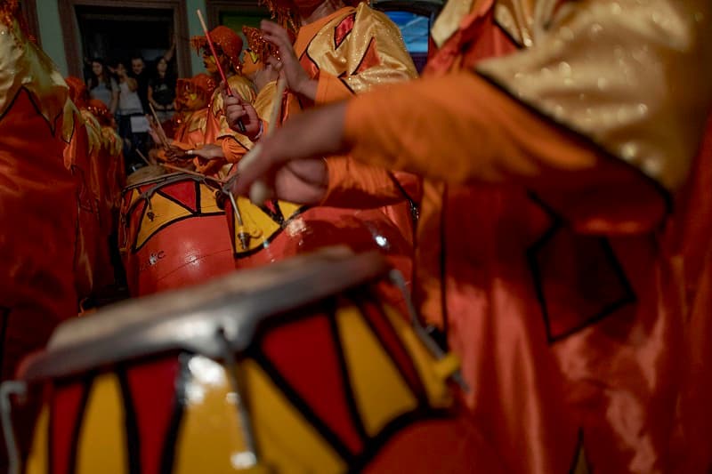 Varias personas tocan tambores pintados de rojo y amarillo en un desfile de llamadas