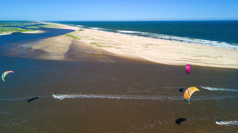 Toma aérea muestar a varios turitas haciendo kite surf en Laguna Garzón, cerca de José Ignacio