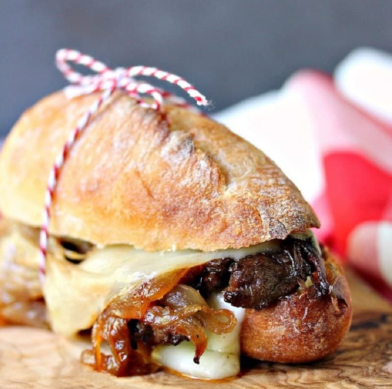 Un chivito de lomo con queso y panceta, entre dos panes caseros atados por un piolín rojo y blanco.