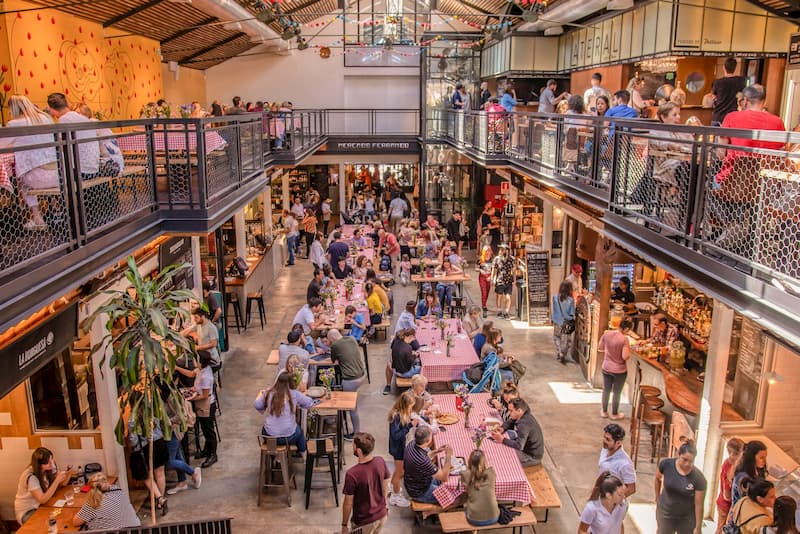 Plano general desde arriba del interior Mercado Ferrando; muchas personas sentadas en mesas