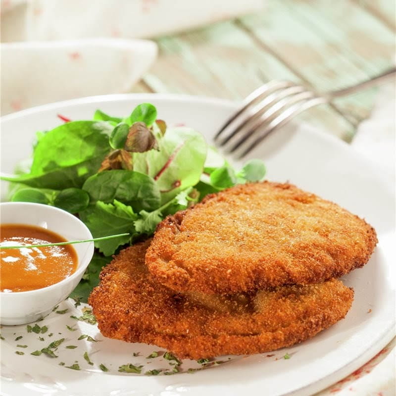 Dos milanesas sobre un plato blanco, acompañadas de ensalada verde y una salsa de color anaranjado