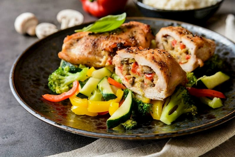 Un plato de pollo relleno, sobre una base de verduras al vapor
