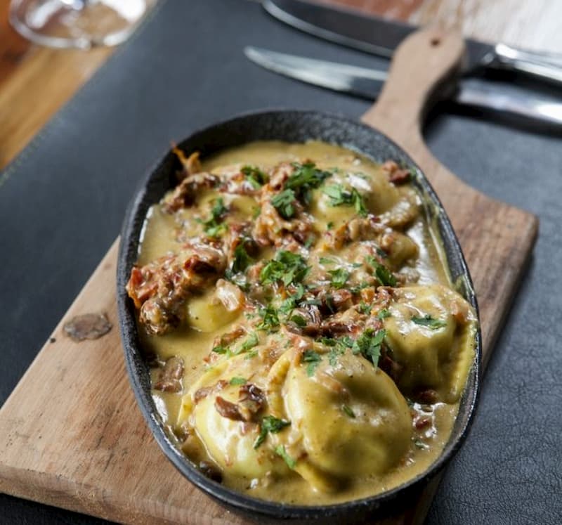 Un plato de sorrentinos con salsa, sobre una tabla de madera